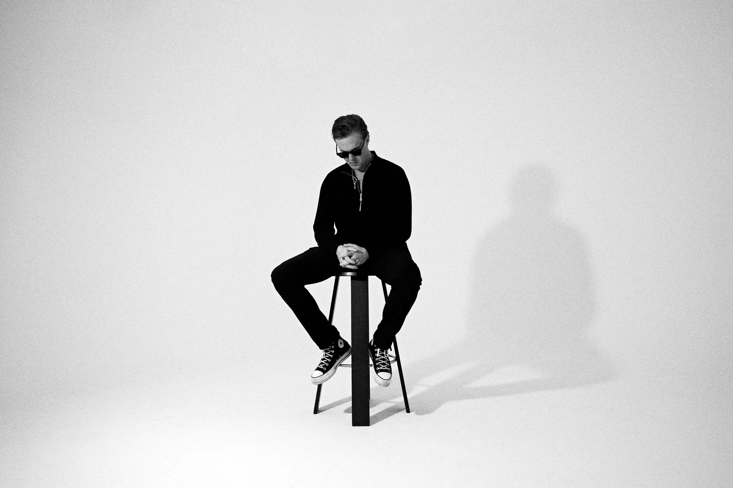 Wide black and white frame of a man seated on a stool in an empty studio
