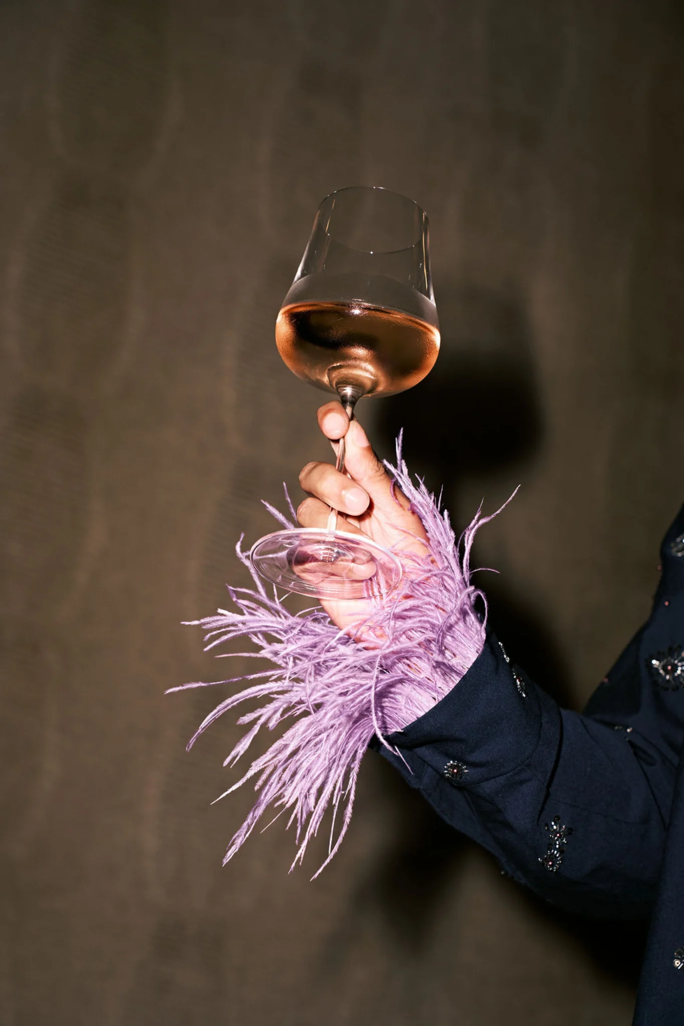Rosé glass held above a lilac feather cuff
