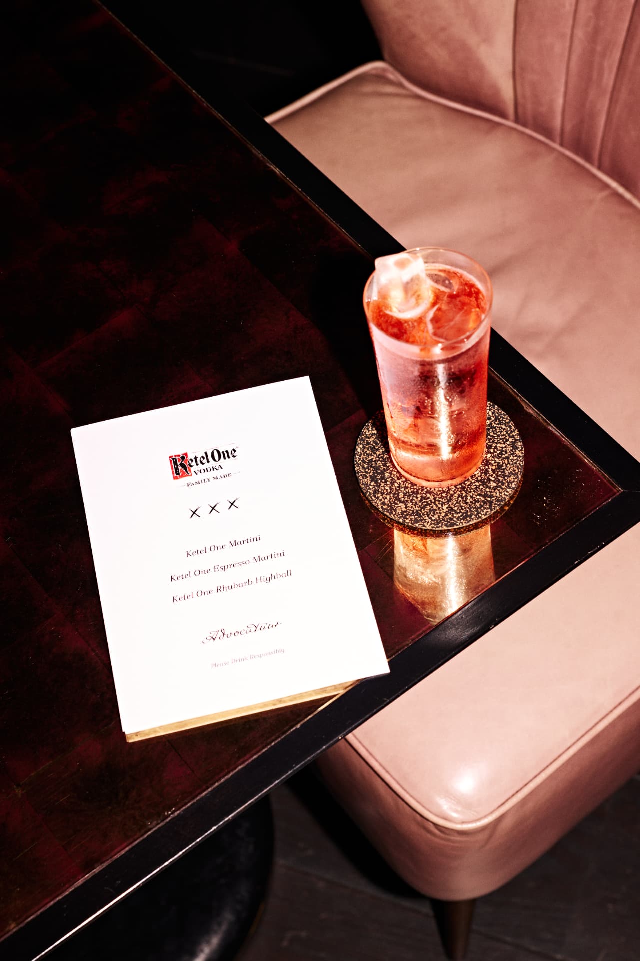 Cocktail and menu beside a velvet banquette