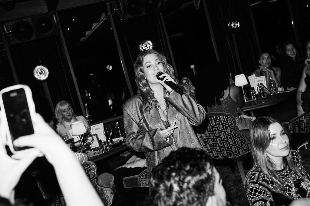 Hiske Bongaarts speaking into a microphone in a sequin blazer, black and white