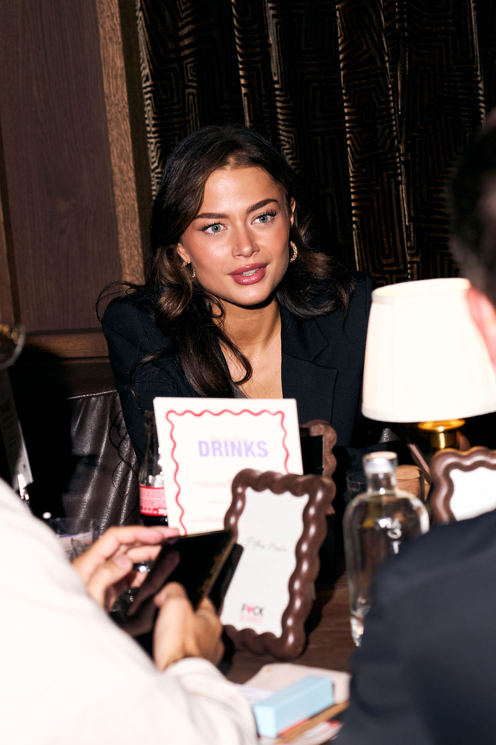 Guest in a black blazer talking across the table beside the drinks card