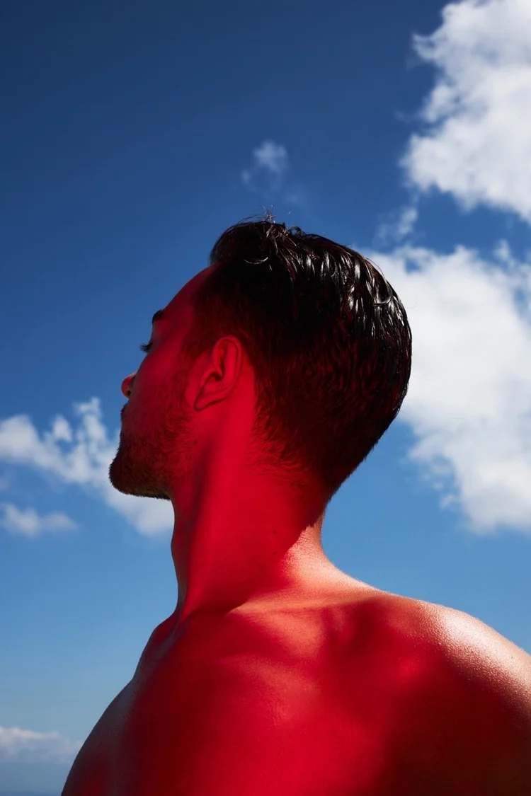 Man against a blue sky lit with hard red light