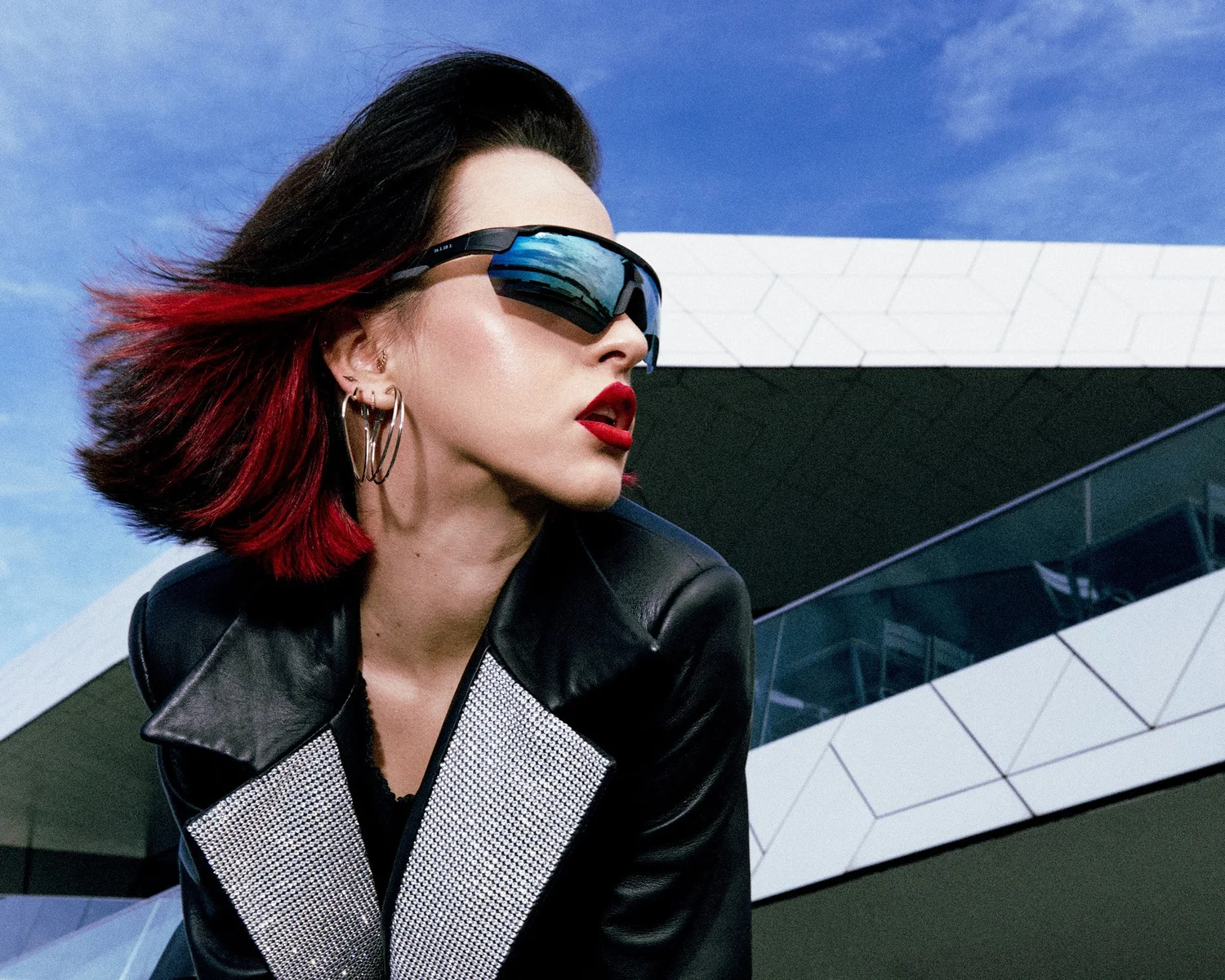 Portrait of a model with red hair and wraparound sunglasses against a blue sky