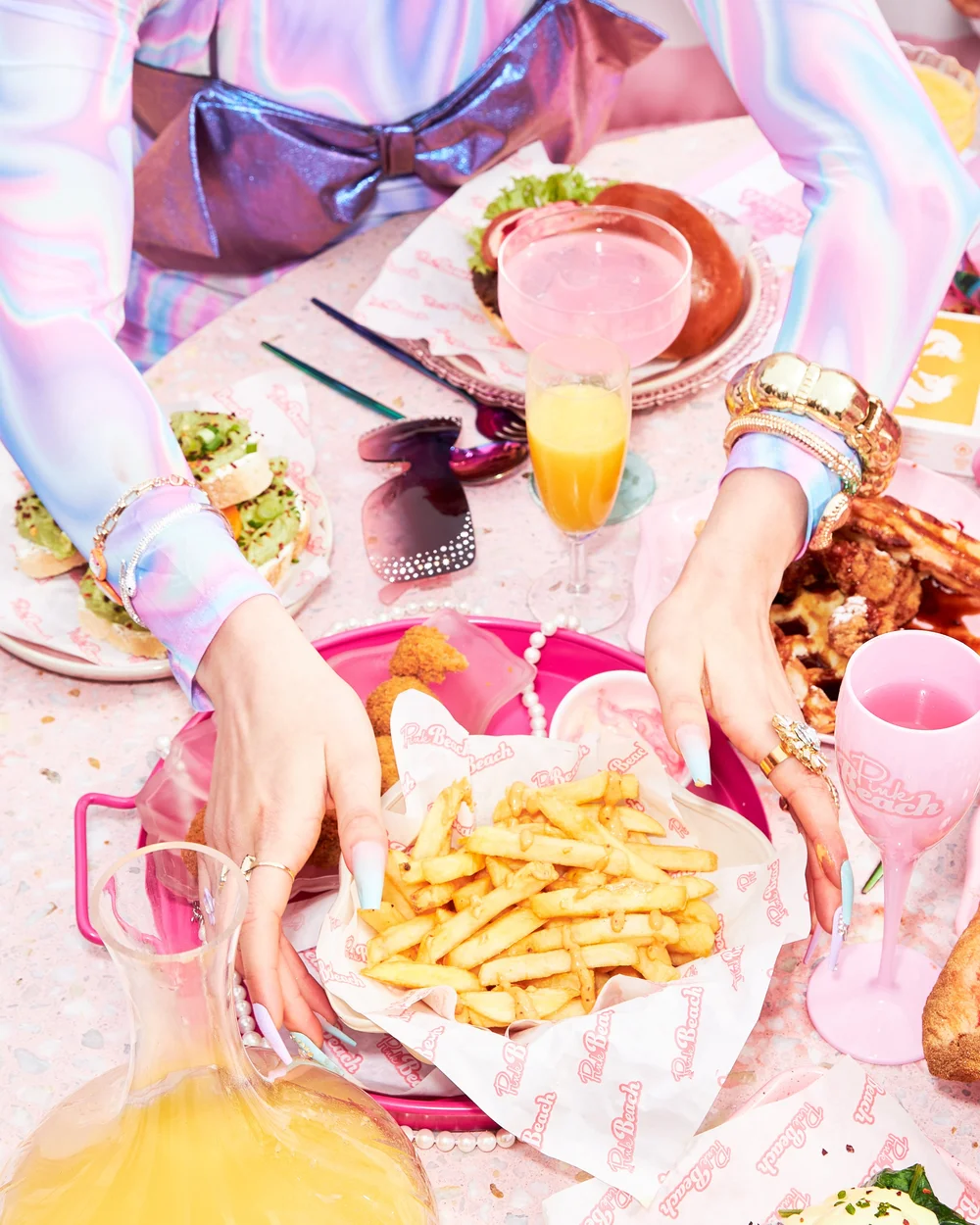 Hands reaching for fries on a pink tray