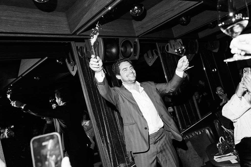 Goof den Hartog raising a sparkler and a glass at the after party, black and white