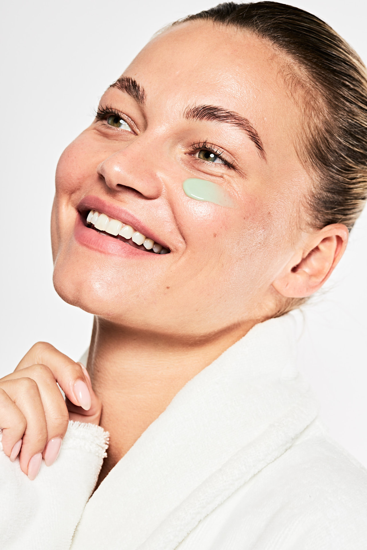 Model in a white robe smiling with cream on the cheek