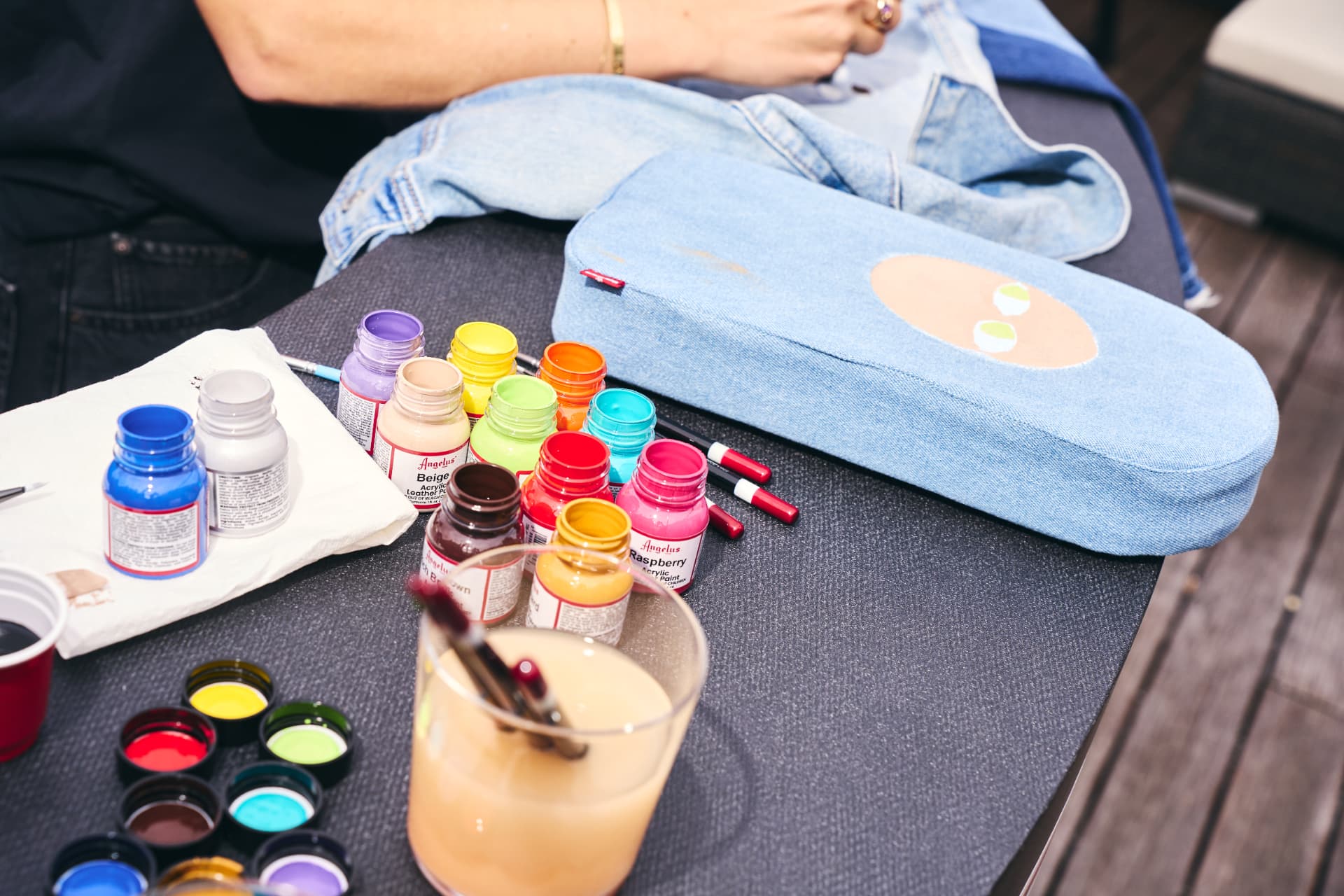 Angelus acrylic paints and brushes on the customisation table beside painted denim