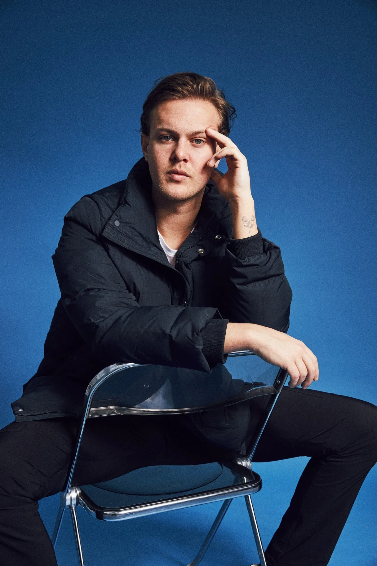 Portrait of Mau seated on a chrome folding chair against blue