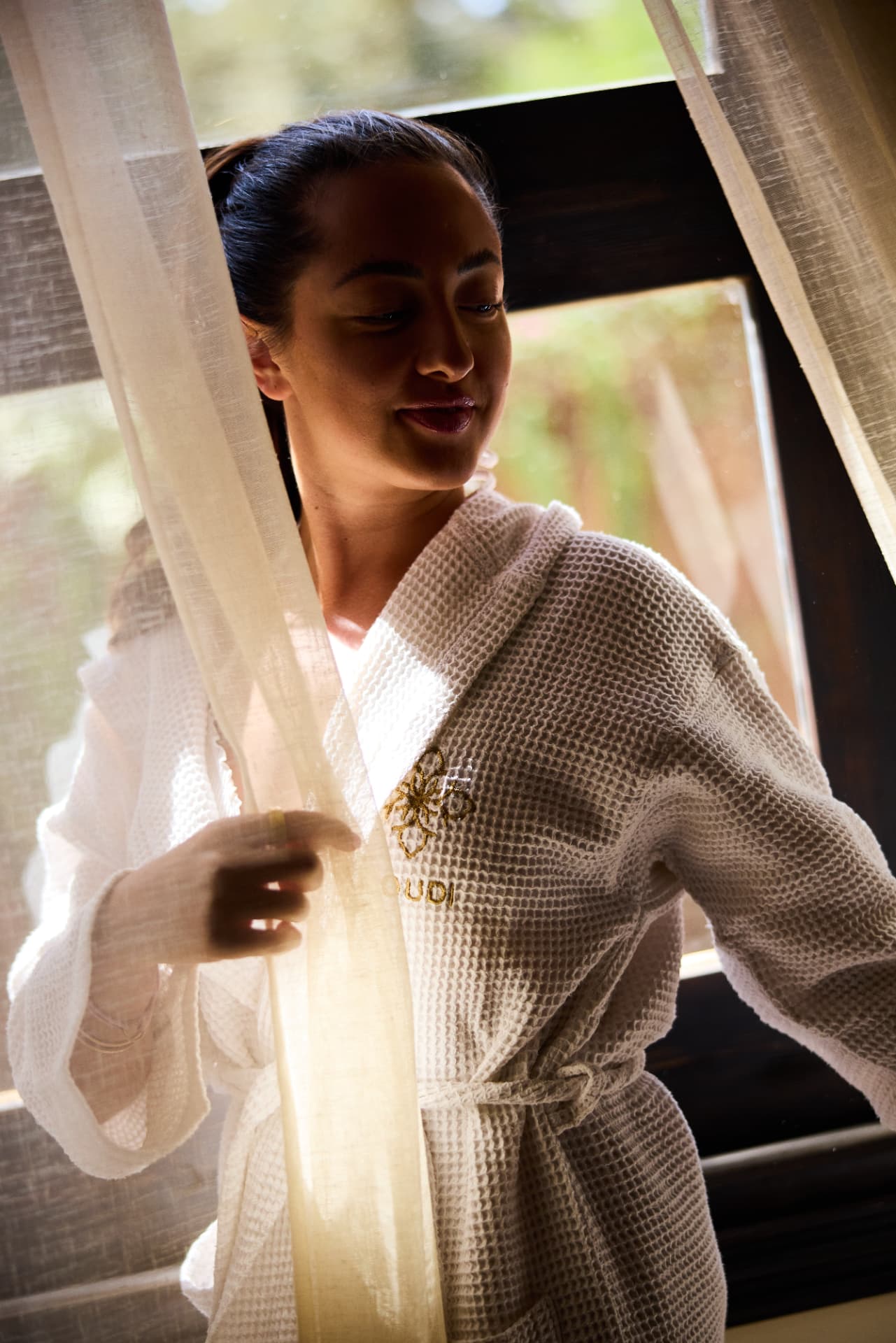 Guest in a white Loudi robe opening the curtain to the morning light