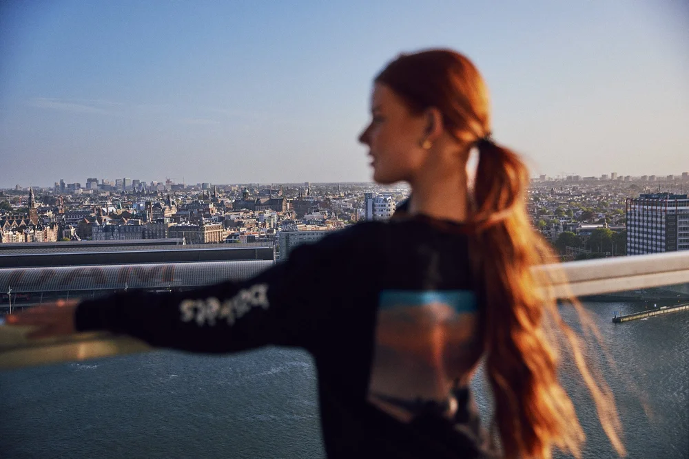 Model at the railing with the Amsterdam skyline behind her