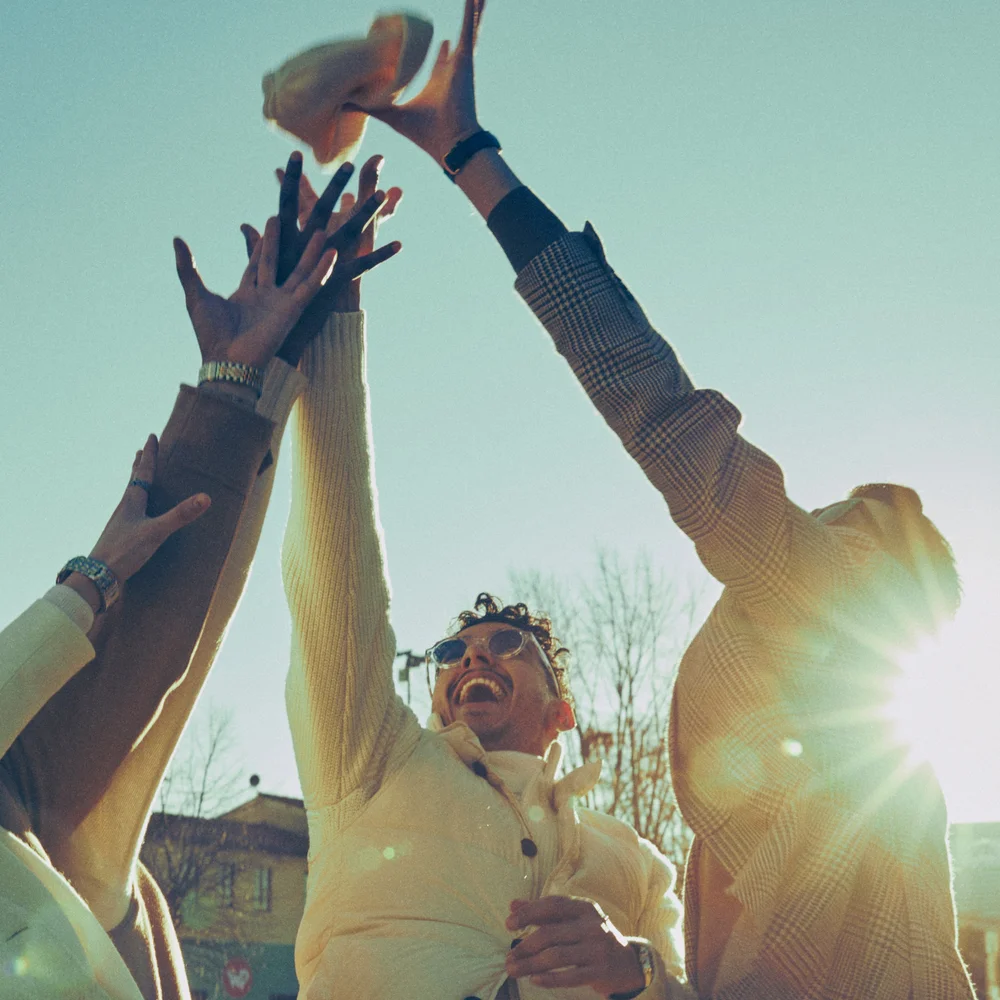 Hands raised catching a hat against the sun