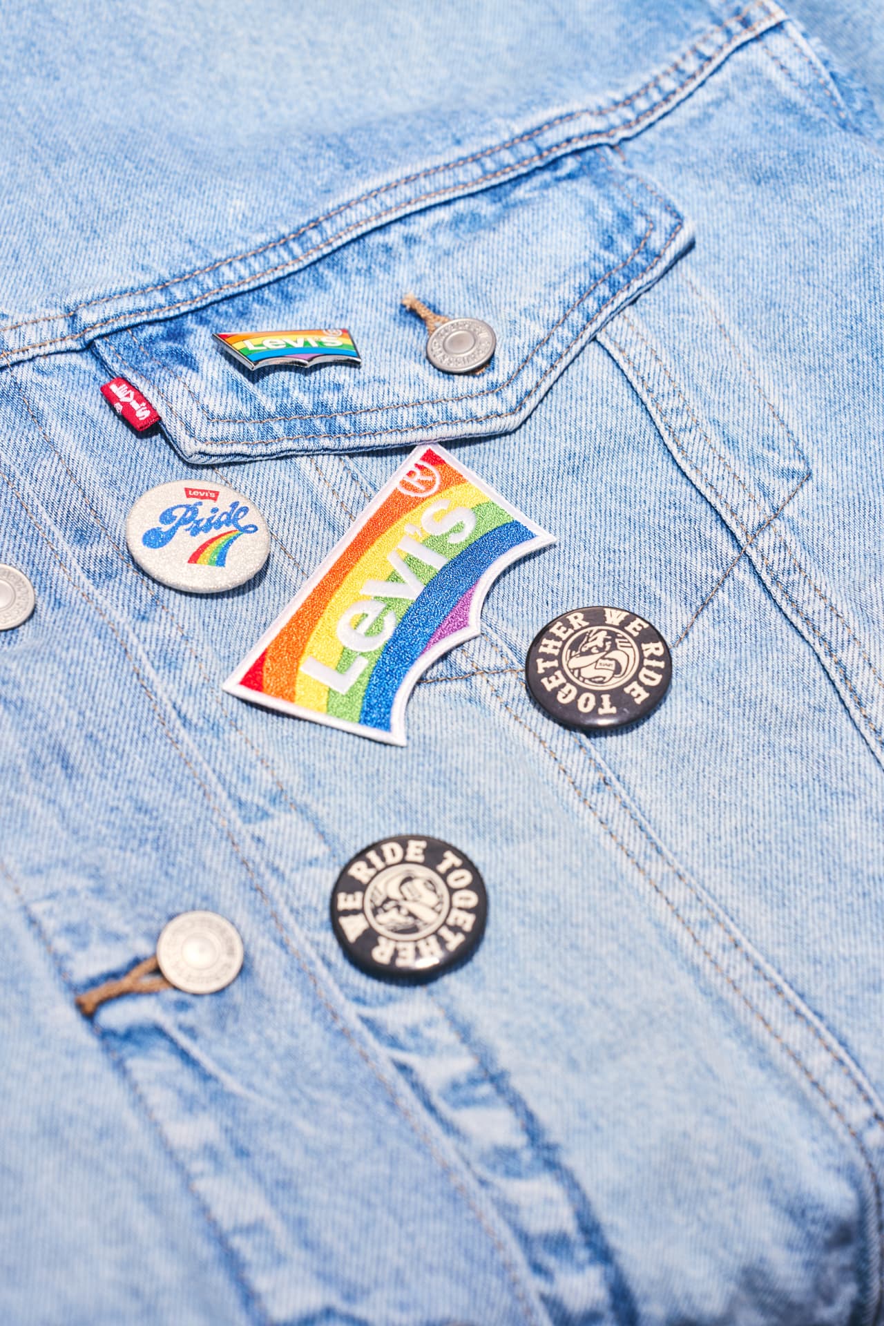 Levi's rainbow batwing patch and Pride pins on a light denim jacket