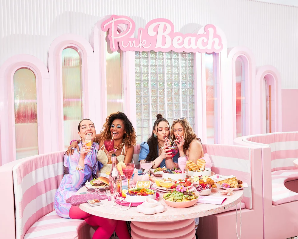 Four women toasting in a pink striped booth under the Pink Beach sign