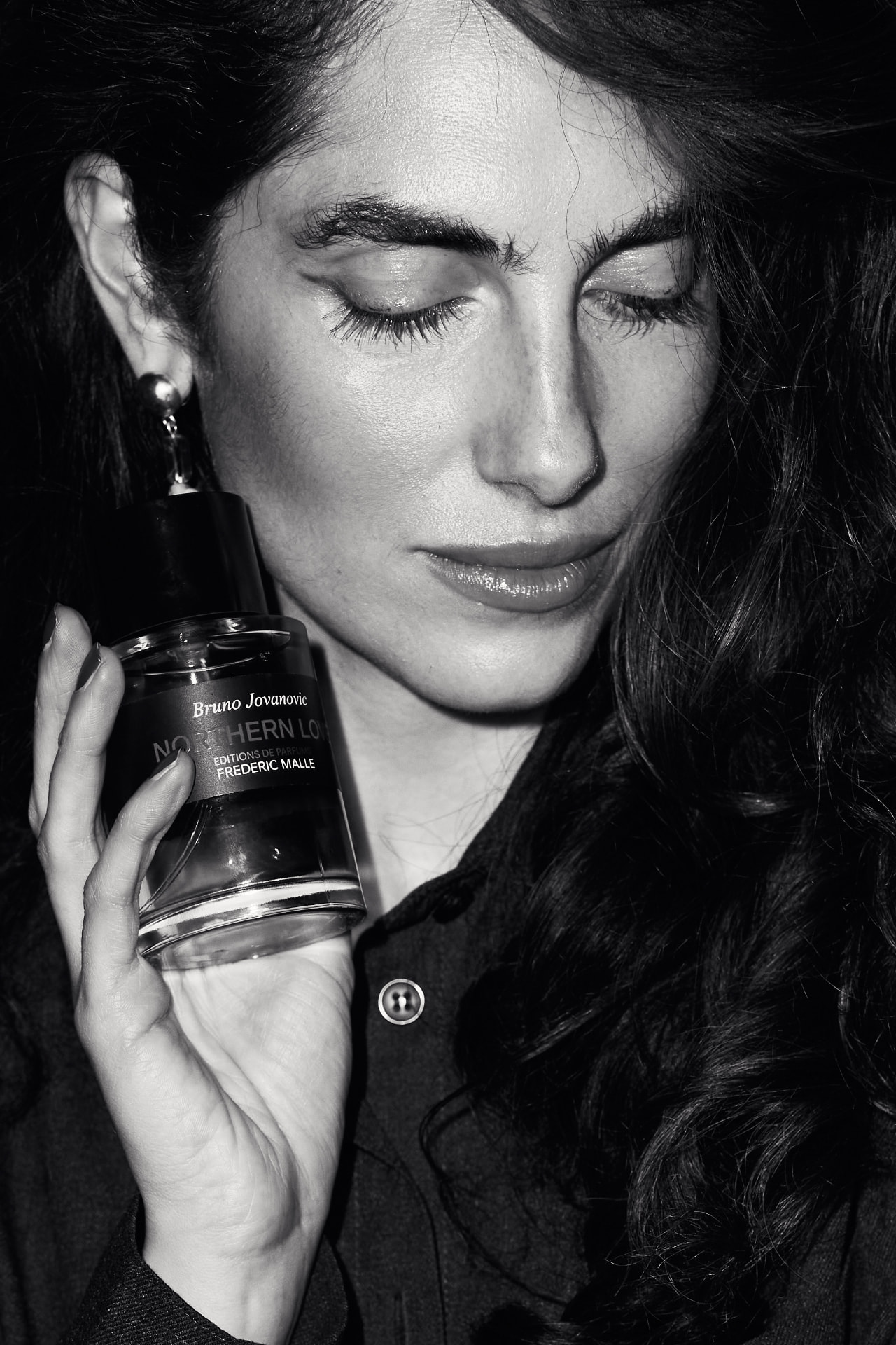 Black and white portrait of a guest holding a Frederic Malle bottle to her cheek
