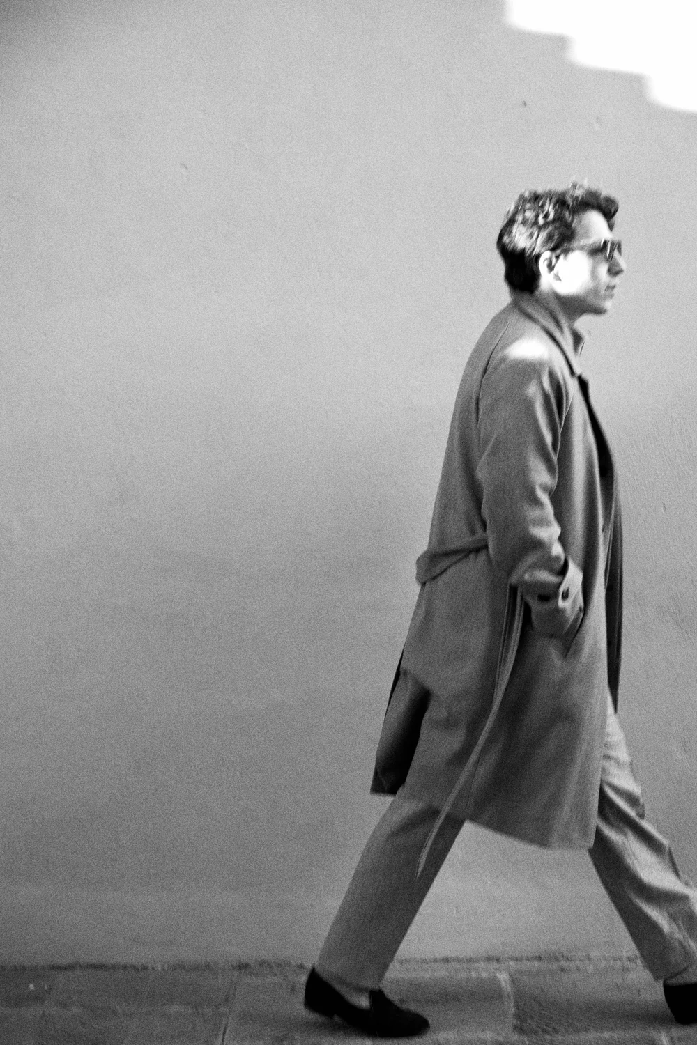Black and white side profile of a man walking in a long coat