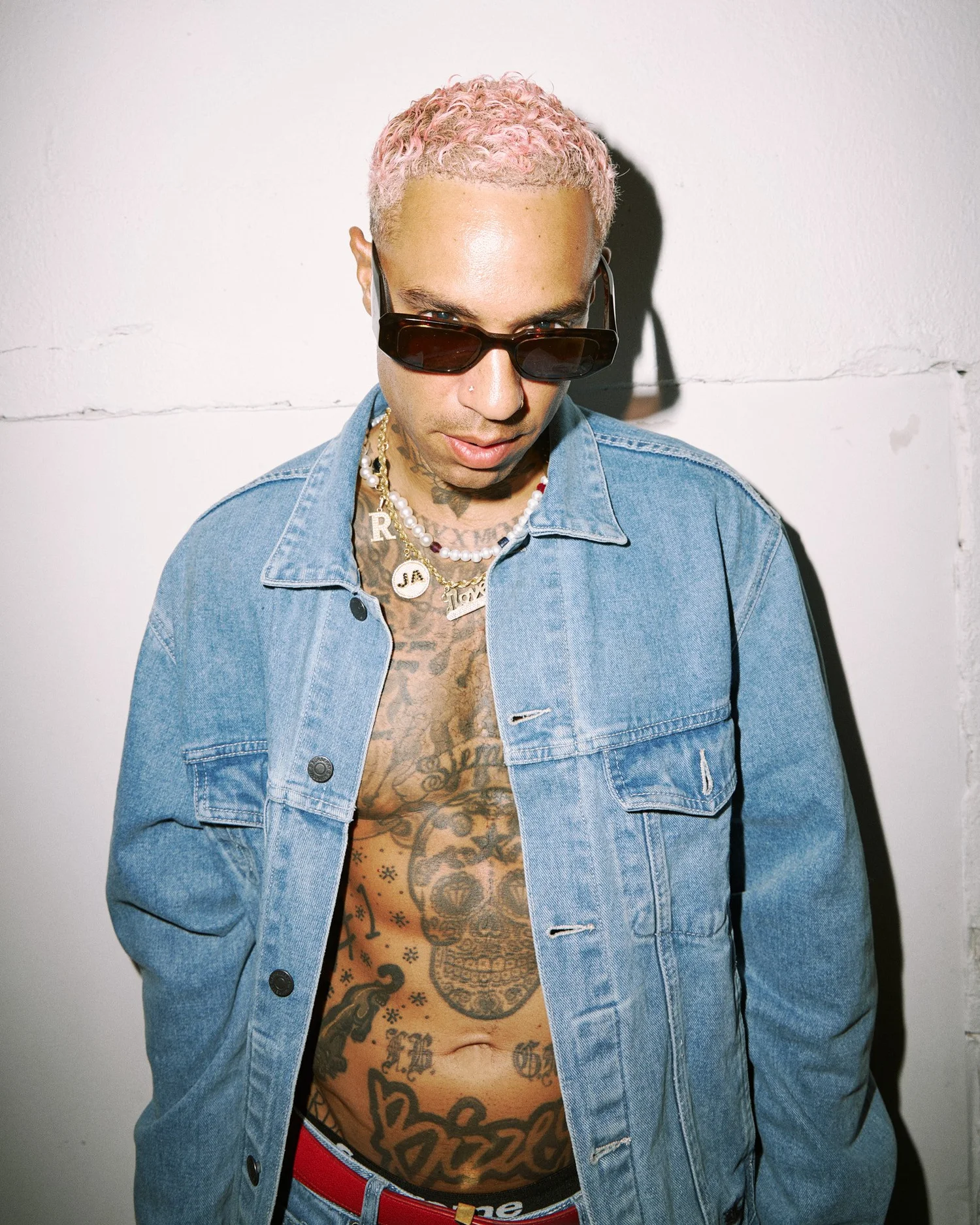 Portrait of Bizzey in a denim jacket against a bare wall