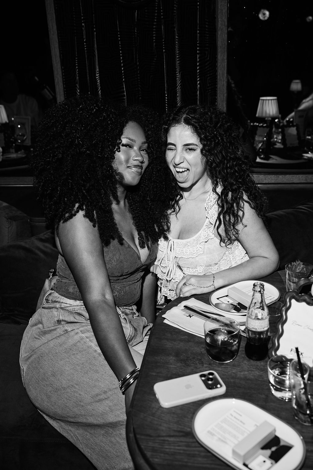 Marwa Omari laughing with a friend on the banquette, black and white