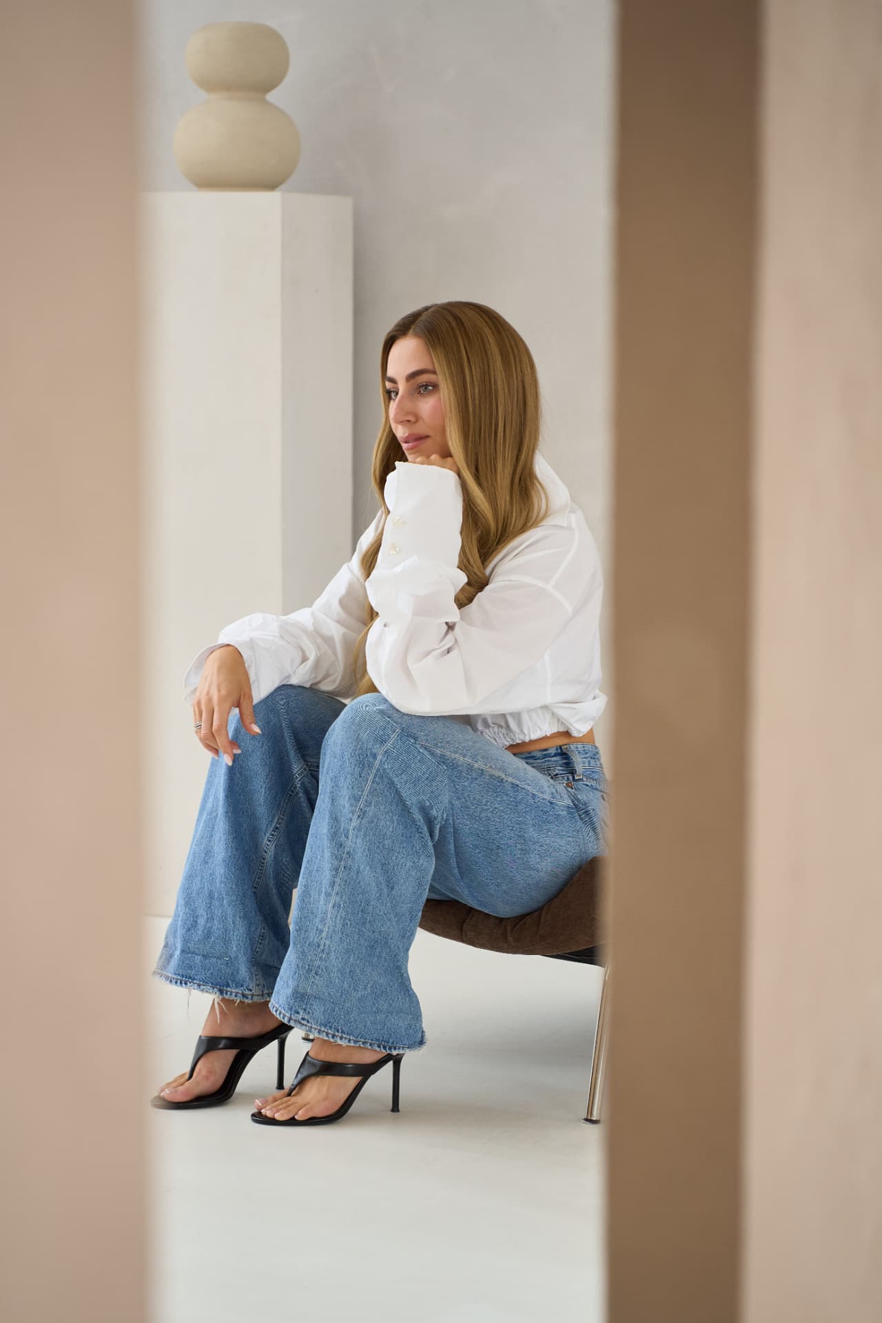 Model in a white shirt and denim seated between plaster columns