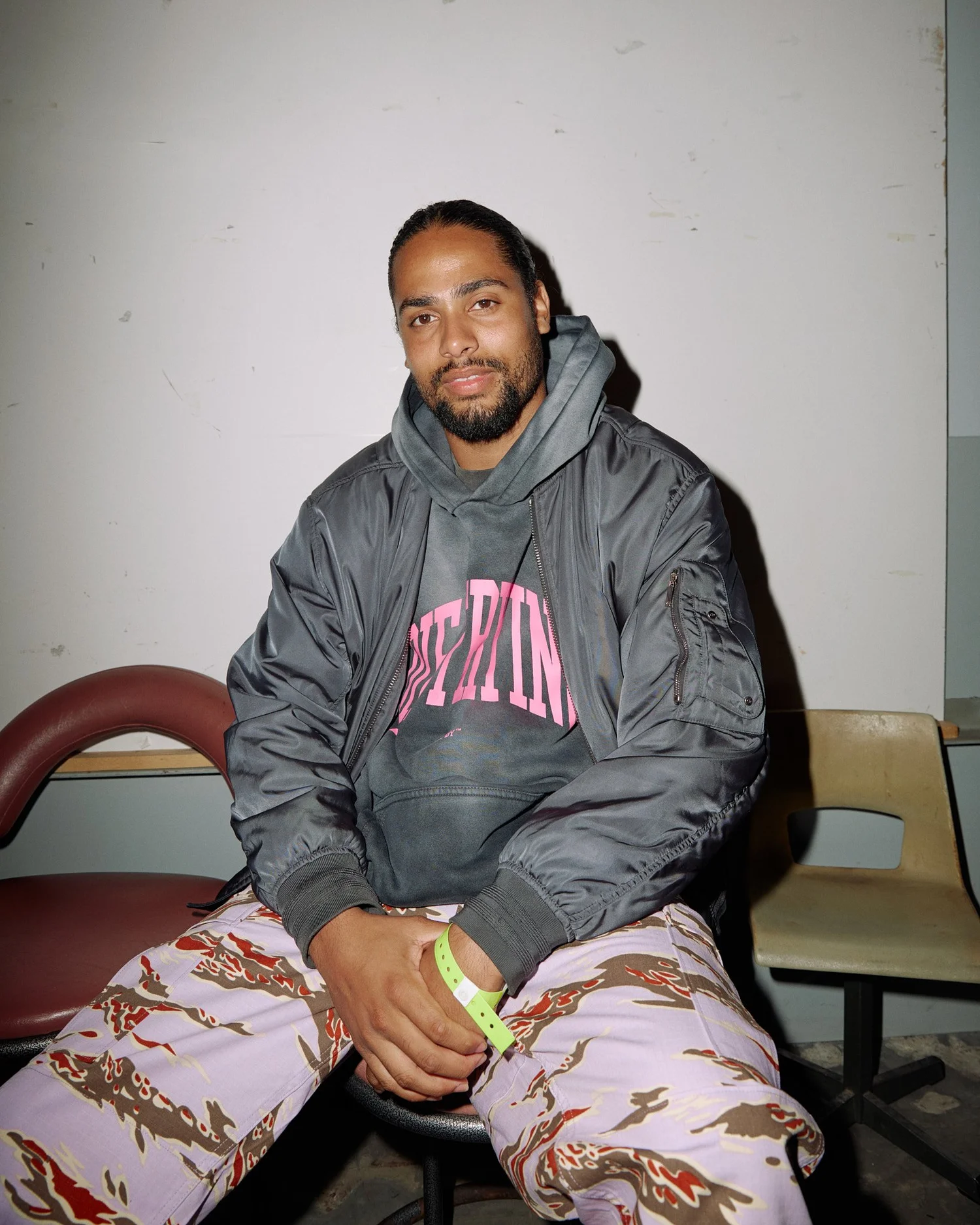 Chai seated on a chair backstage in a bomber jacket