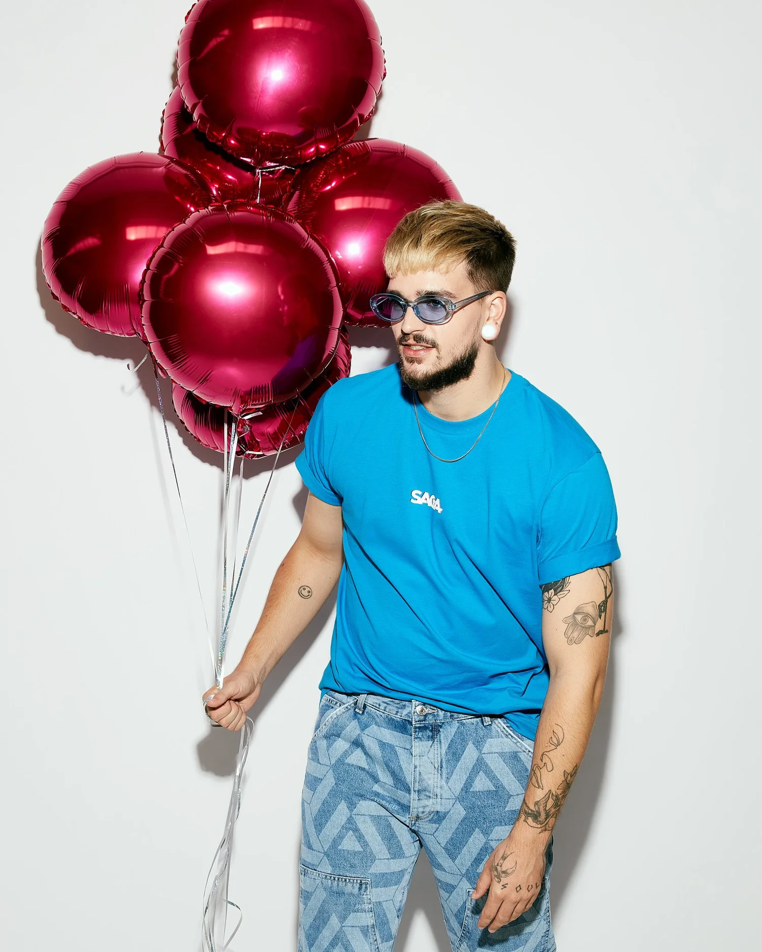 Model in a blue SAGA tee holding a bunch of magenta foil balloons
