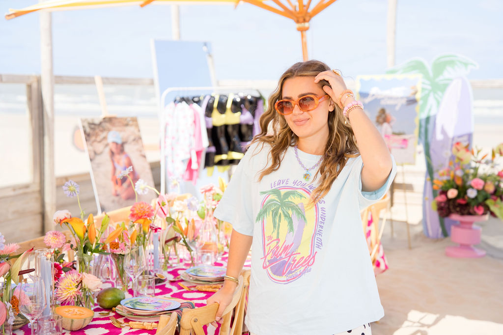 Host in a printed tee beside the beach table