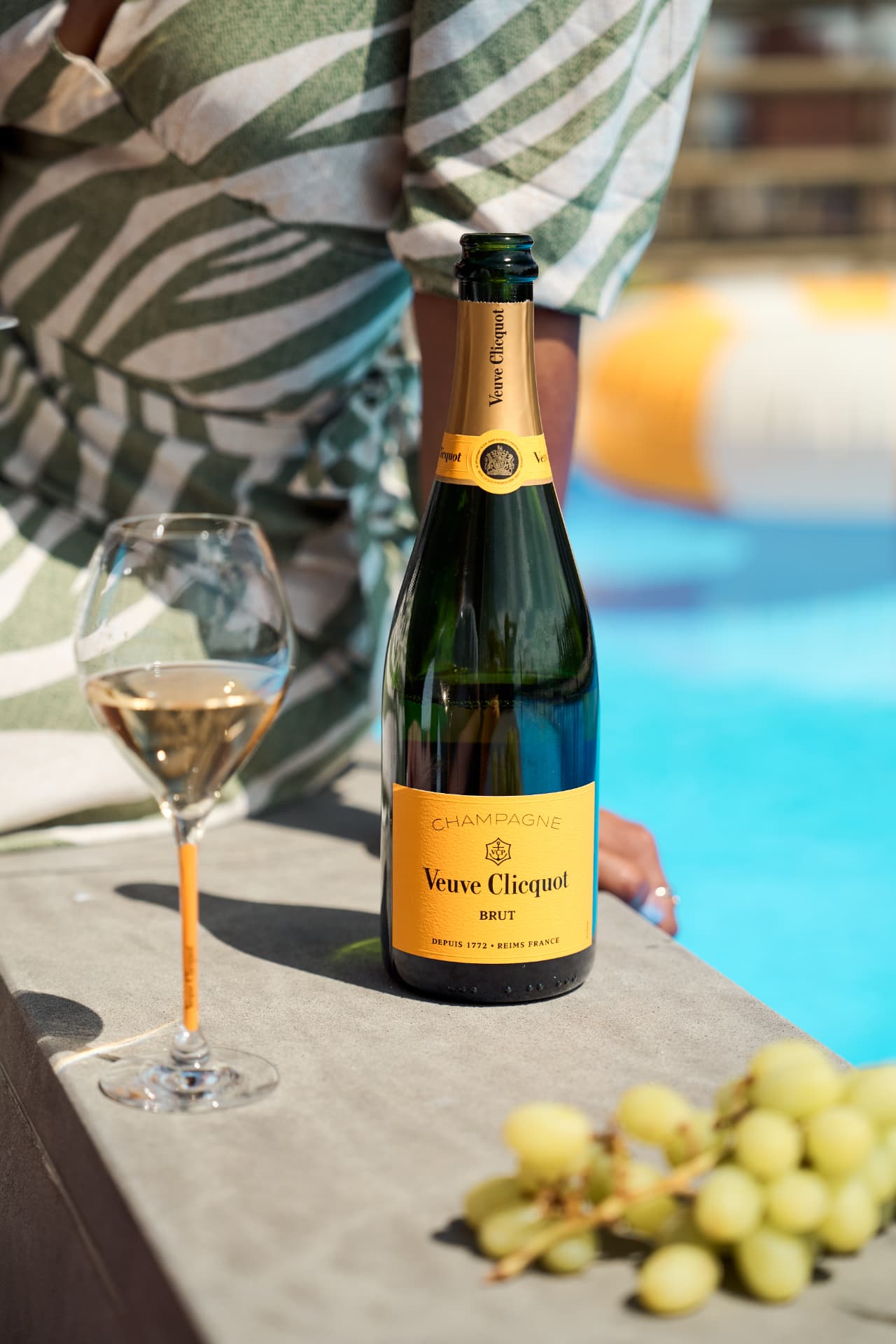 Brut bottle and glass on the pool edge with grapes