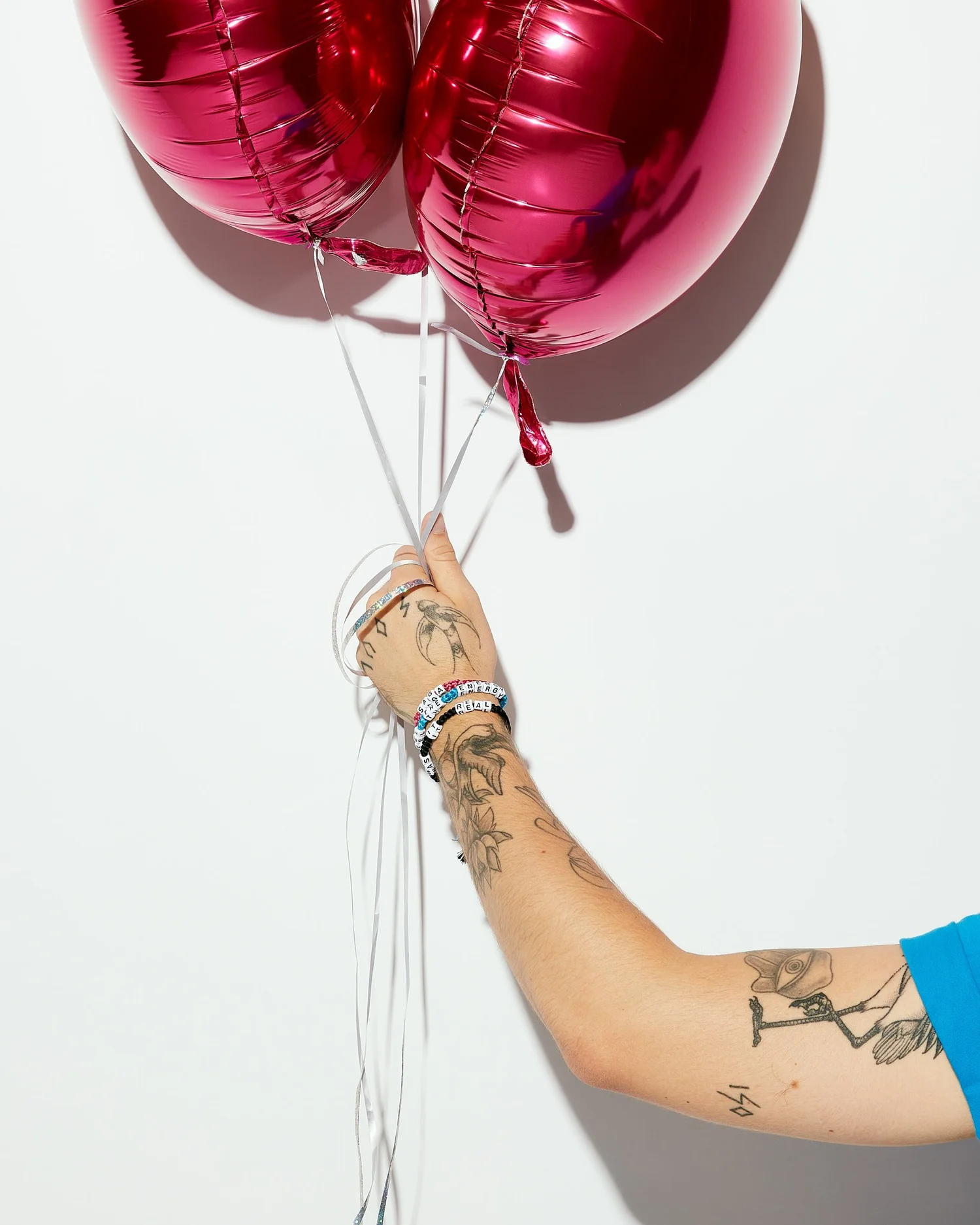 Tattooed arm holding magenta foil balloons against white