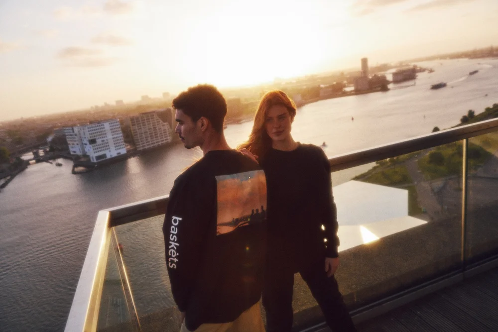 Two models in black A'DAM&Co sweaters on the rooftop with the IJ behind them