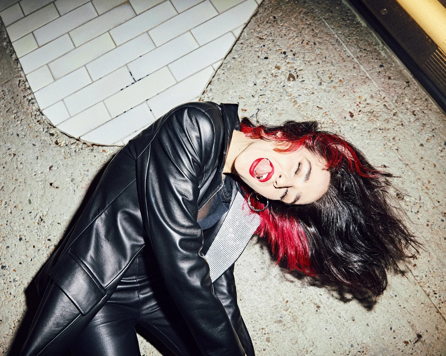 Model lying on concrete in a leather coat, hair fanned out