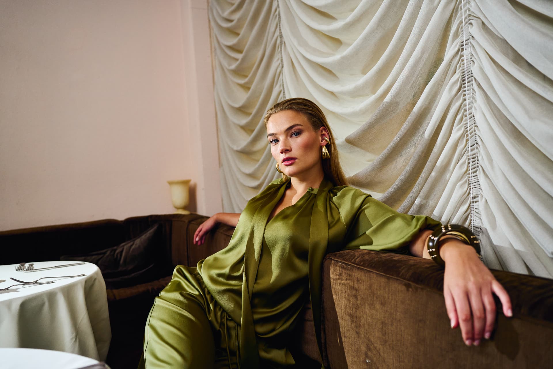 Model in olive satin seated on a brown velvet sofa