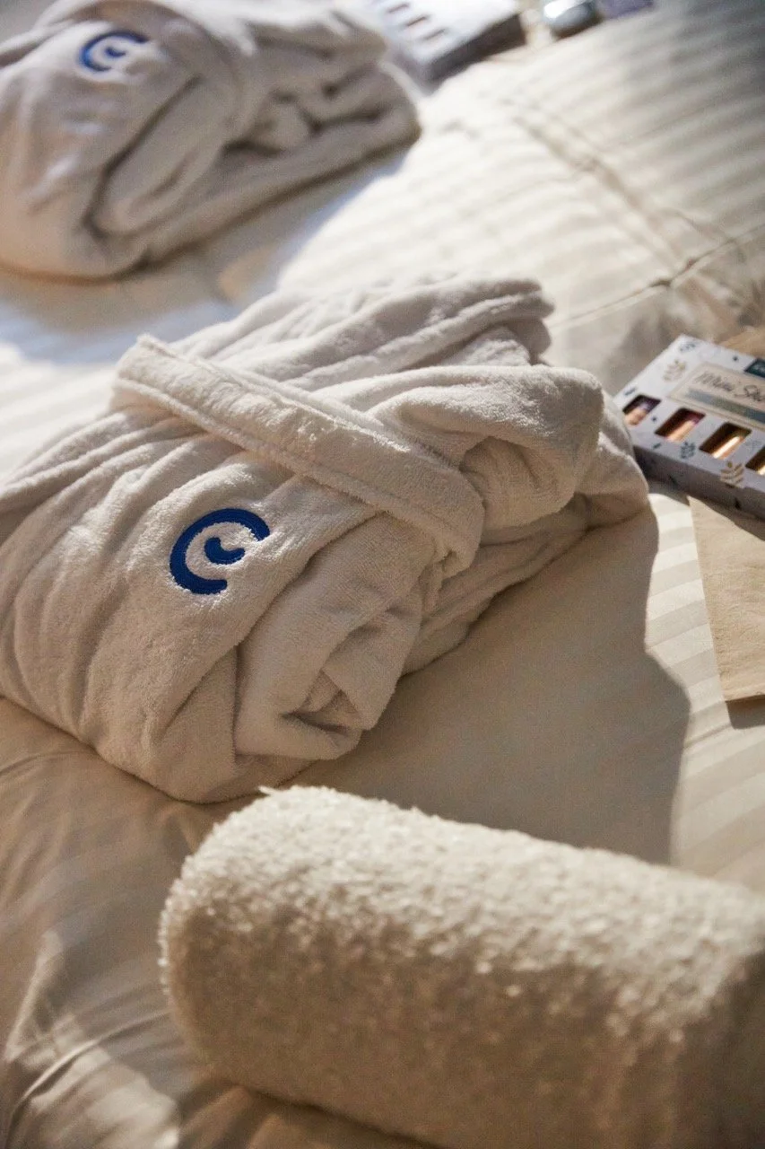 Rolled Emma robes and towels laid out on a made bed