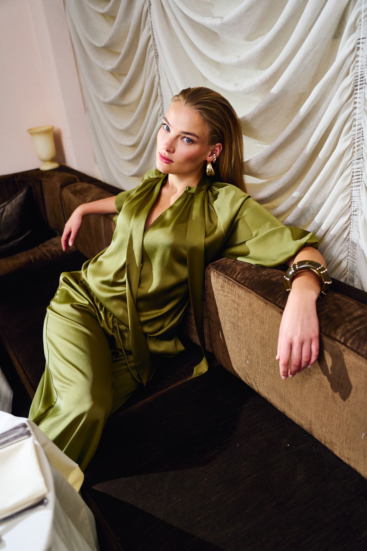 Model in olive satin seated against draped linen