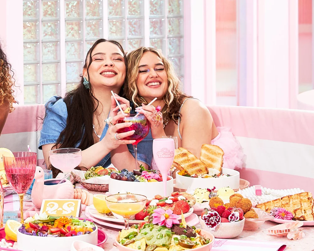 Two women laughing over a loaded brunch table