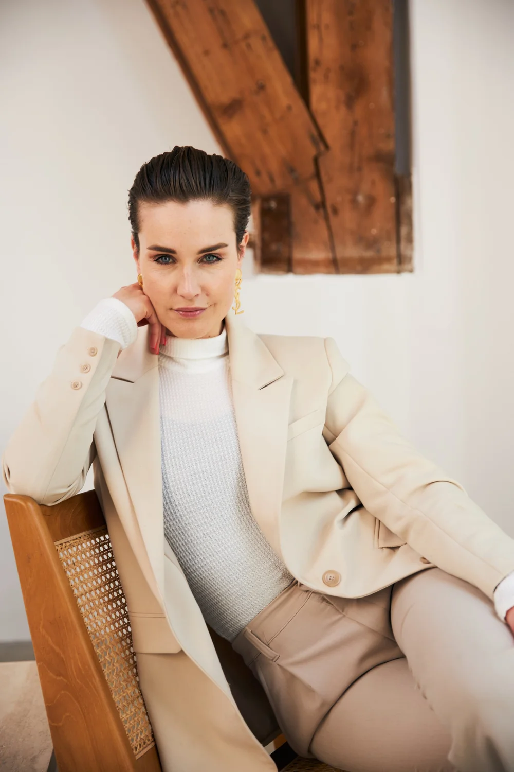 Woman in a bone suit seated on a cane chair under a wooden beam