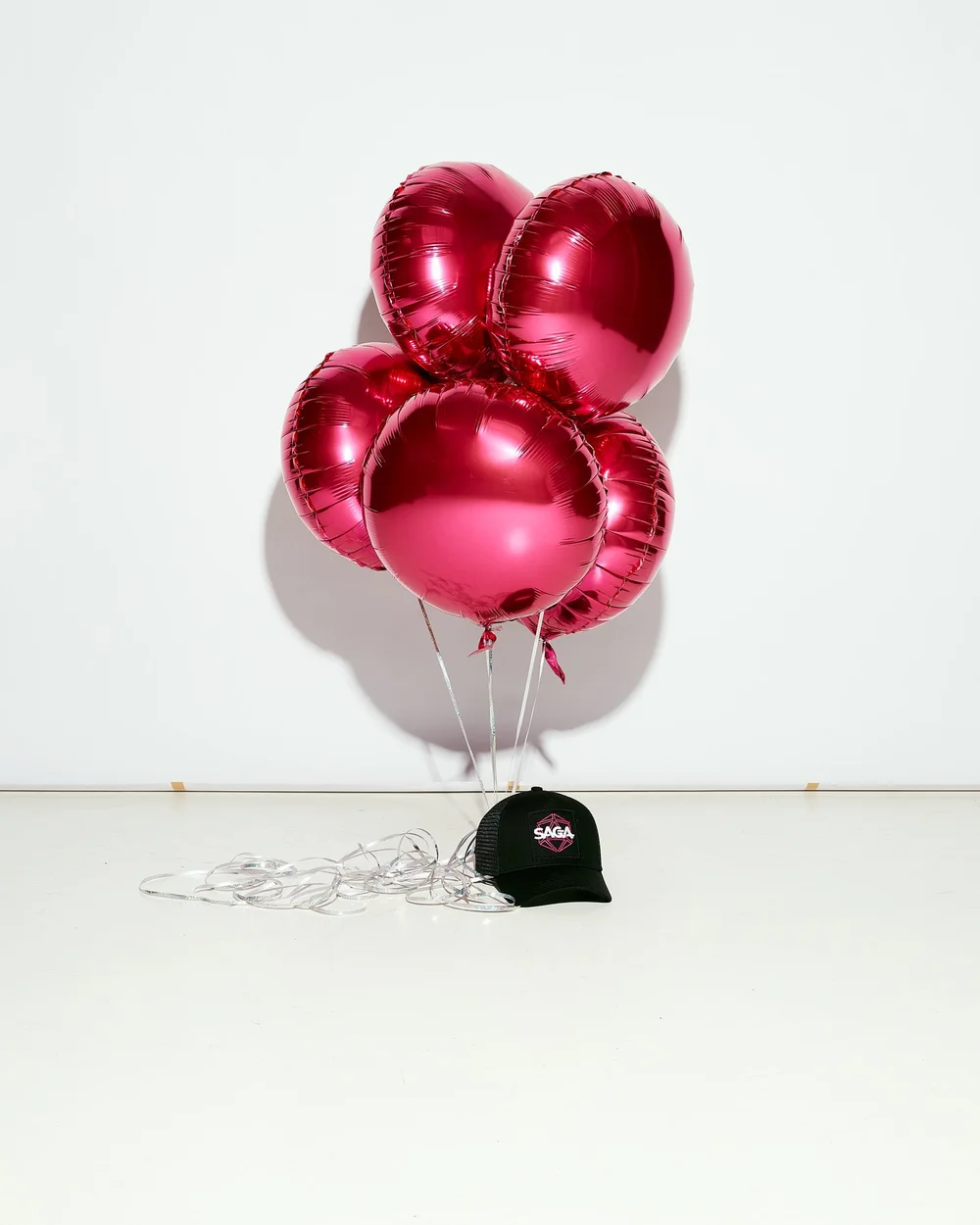 Still life of magenta balloons and a black SAGA cap on the floor