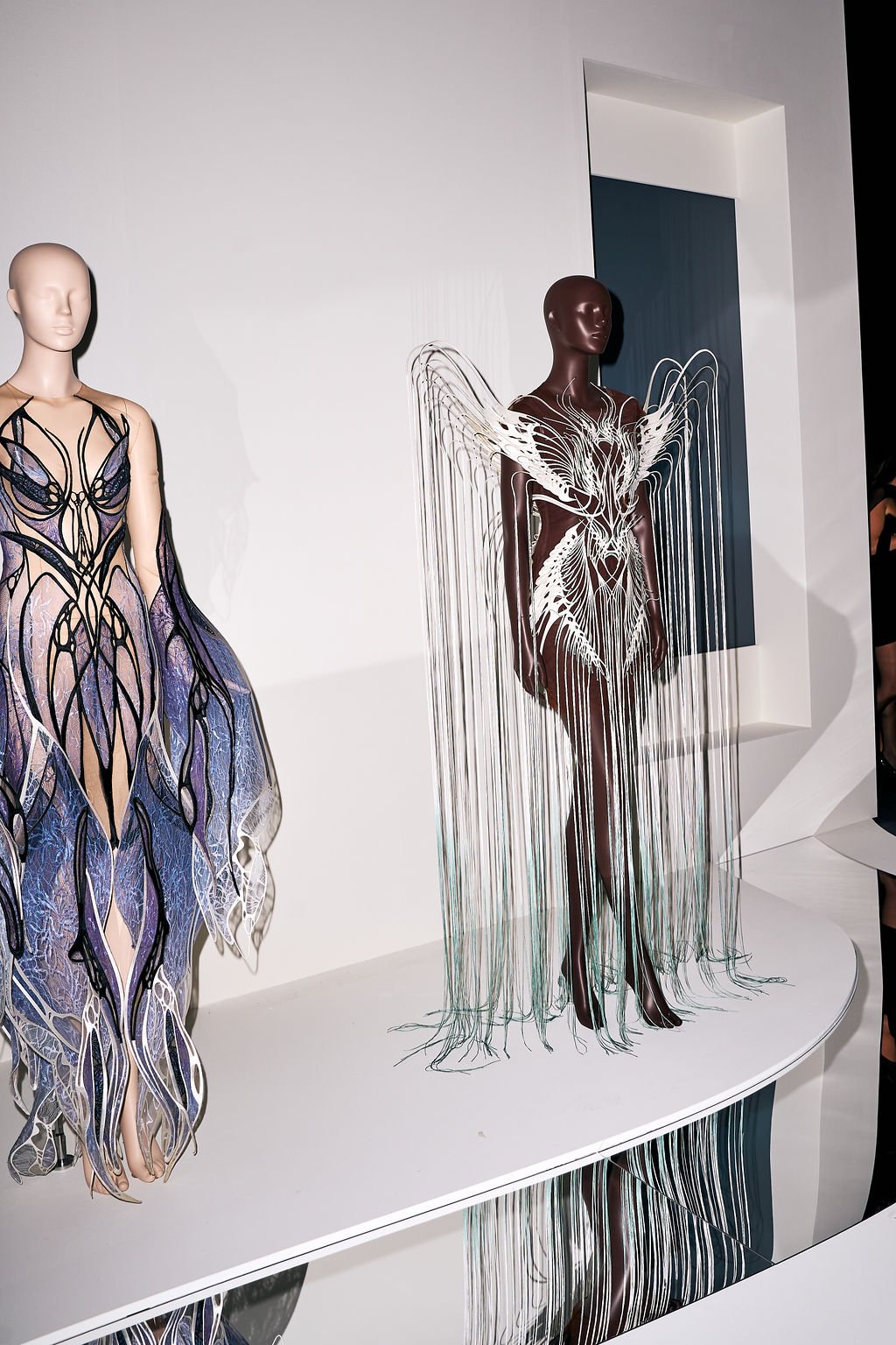 Two gowns on a curved white plinth, one trailing fine strands