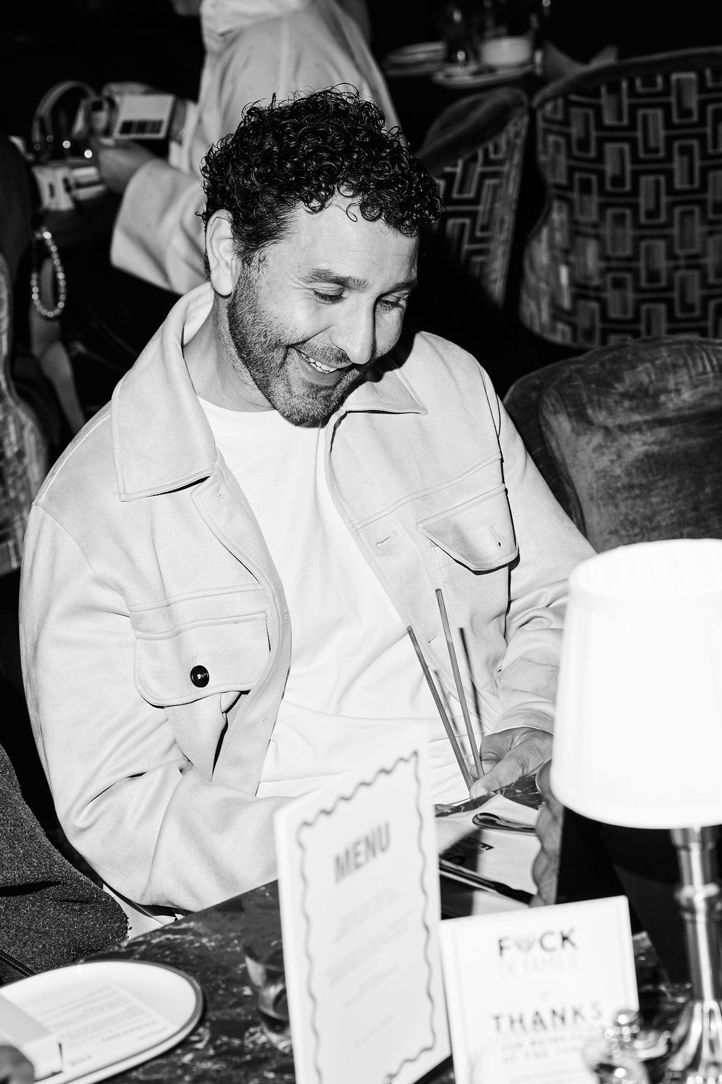 Guest in a cream jacket smiling over the menu card, black and white