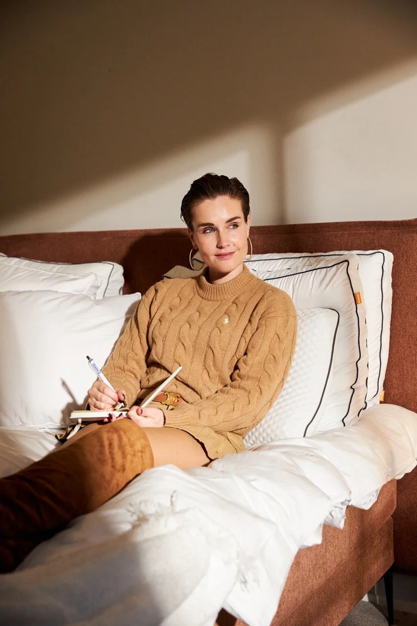 Woman in a camel sweater writing in a notebook on the bed