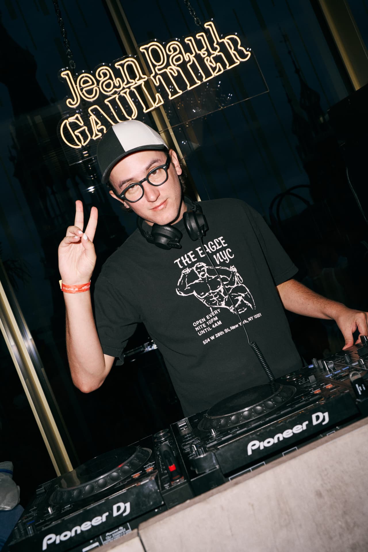 DJ in a cap making a peace sign behind the booth